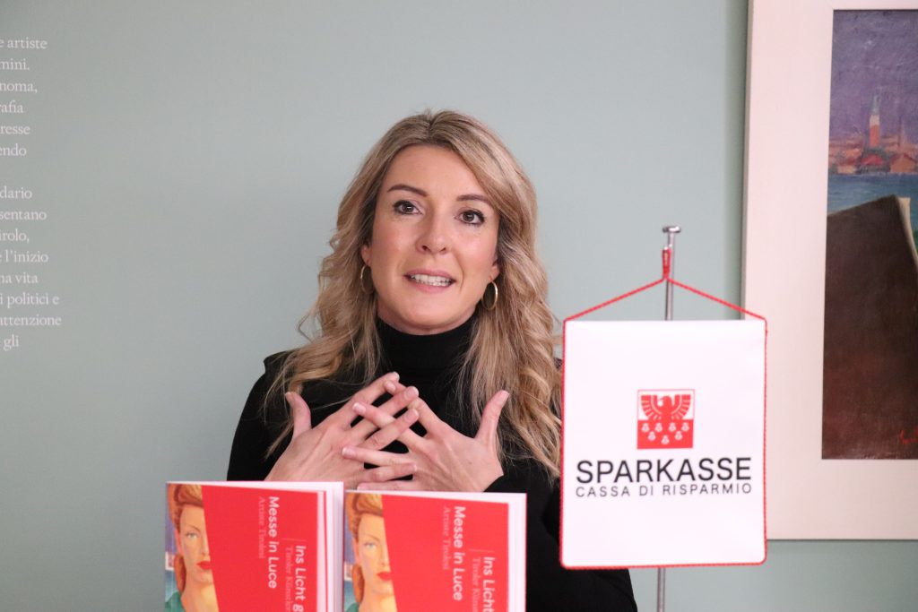 Lisa Trockner mit zwei roten Büchern und einem Banner mit dem Logo und dem Schriftzug „Sparkasse“ vor sich