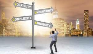 Mann vor einem Schild mit der Aufschrift „Volatility, Uncertainty, Complexity, Ambiguity“ und im Hintergrund eine Skyline